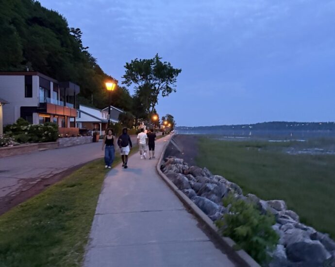 People walking beside the St. Lawrence River at dusk on the Jacques-Cartier Beach promenade in Cap-Rouge