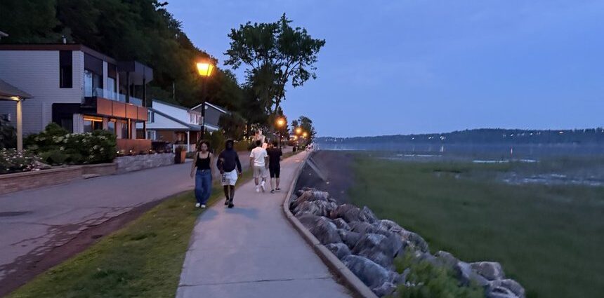 People walking beside the St. Lawrence River at dusk on the Jacques-Cartier Beach promenade in Cap-Rouge
