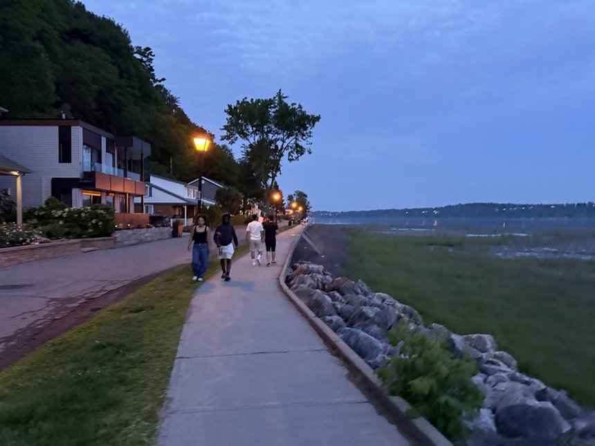 People walking beside the St. Lawrence River at dusk on the Jacques-Cartier Beach promenade in Cap-Rouge