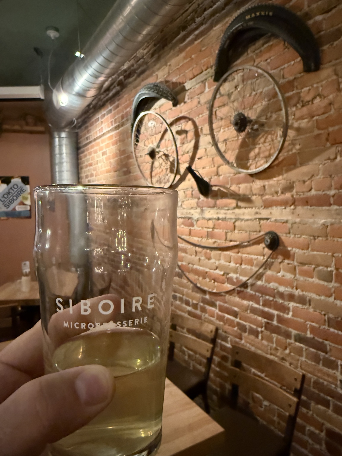 A Siboire glass in front of decorative bicycle wheels mounted on an exposed-brick wall at Siboire Saint-Vallier